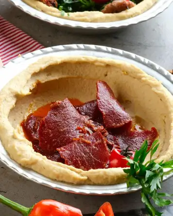 Pastırmalı humus, kremamsı humus üzerinde baharatlı pastırma dilimleri ile servis edilen Hatay usulü lezzet