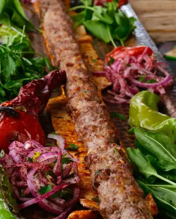 Hatay usulü Vezir kebabı, şişte pişirilmiş baharatlı kıyma kebabı, közlenmiş sebzeler ve sumaklı soğan ile servis edilir